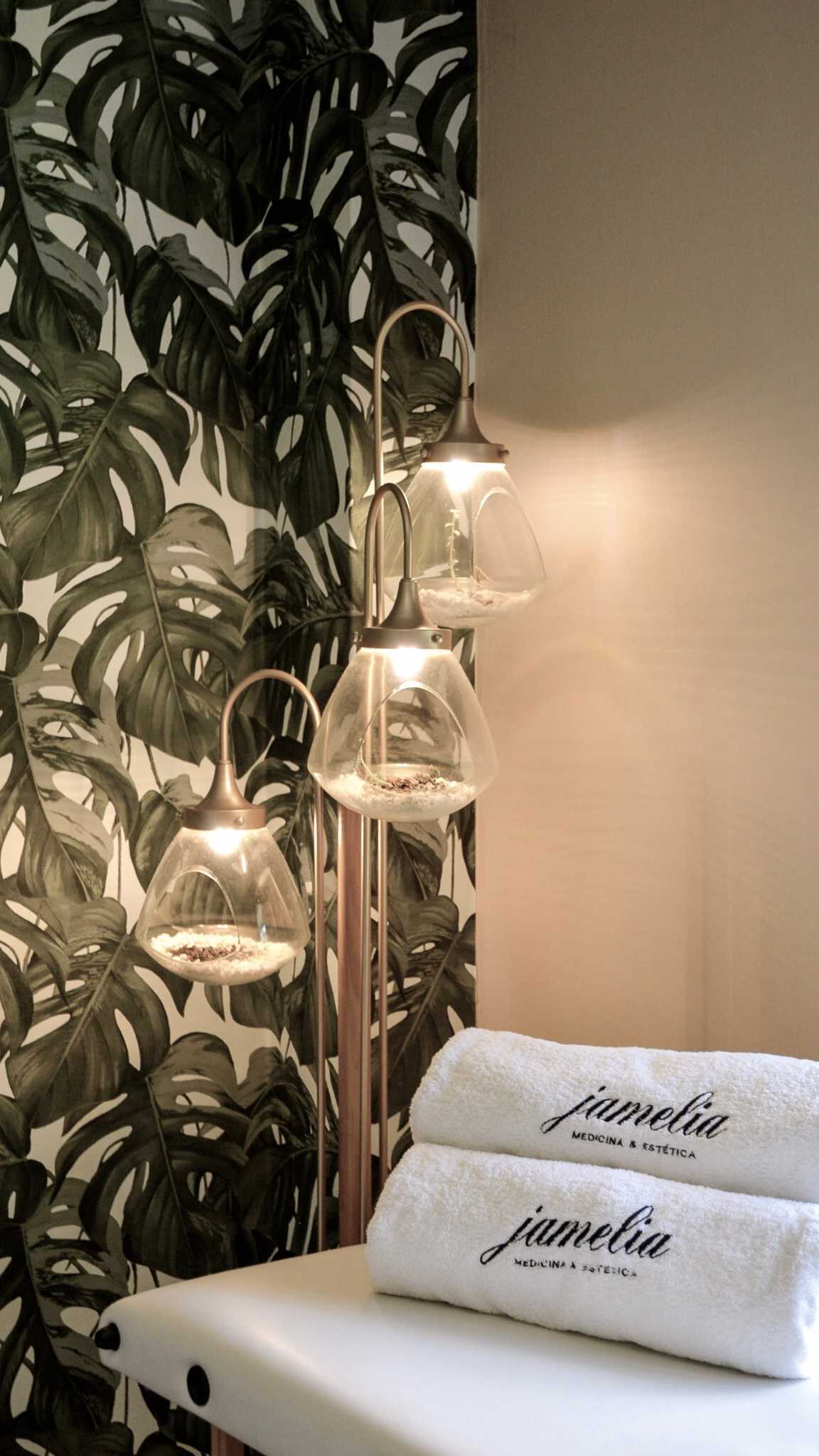 Cabina con papel de monstera, lámparas de cobre y toallas bordadas con el logo